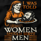 T-shirt design with a graphic of a woman holding a head and text 'I was told women should serve men' on a black background.